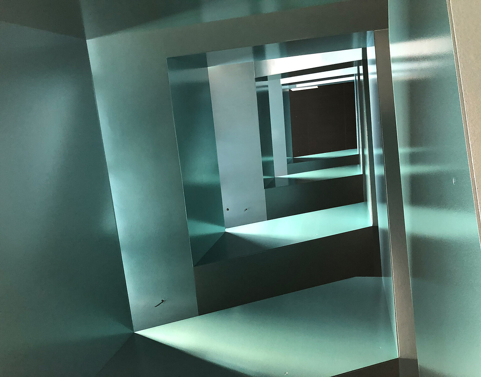 Innenaufnahme eines modernen, geometrisch gestalteten Treppenhauses mit rechteckigen Öffnungen und kühlem, bläulichem Licht.