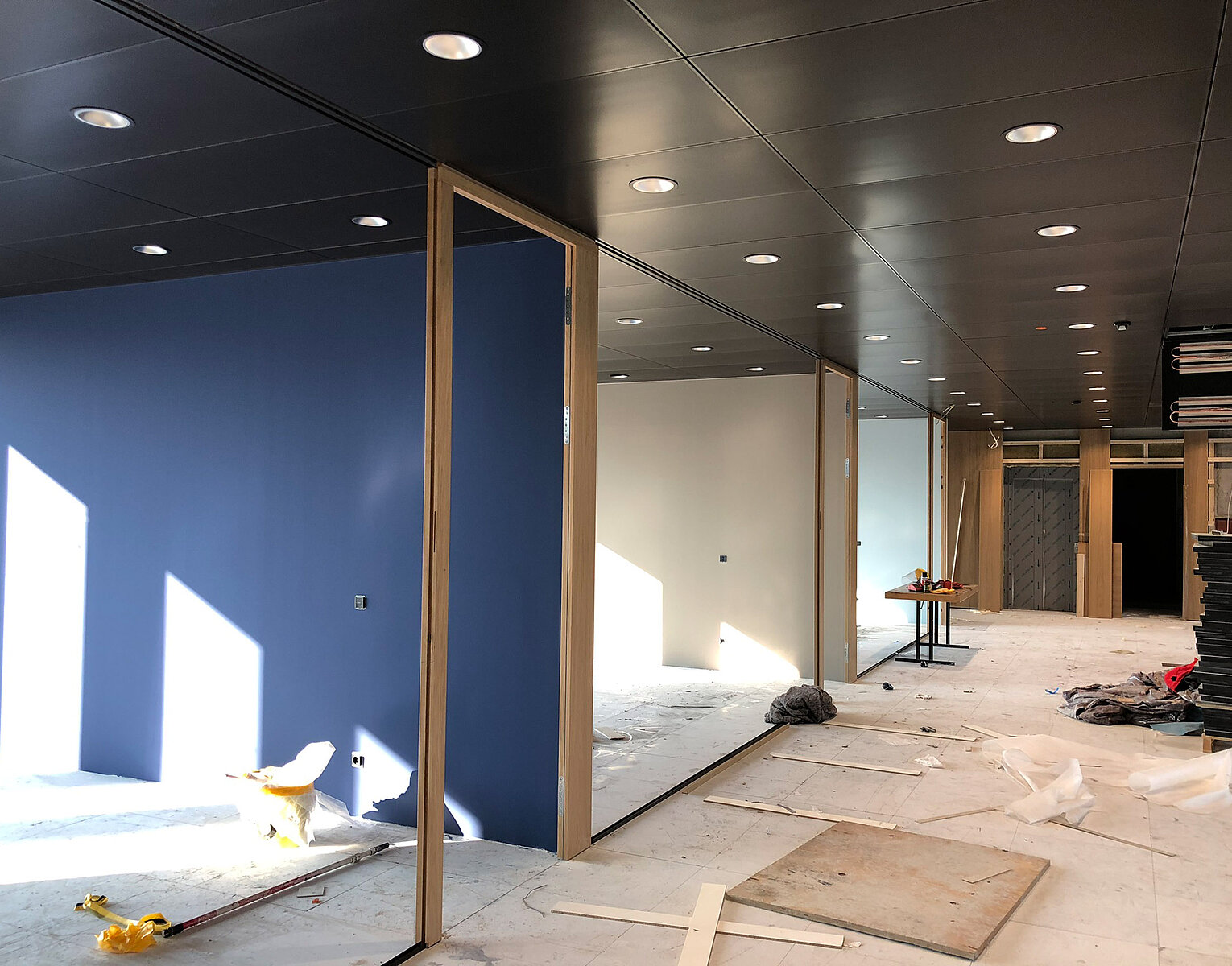 Innenraum in Umbau mit blauer Wand, Spiegeln, Baustoffen und Werkzeugen auf dem Boden und Decke mit eingebauten Lampen.