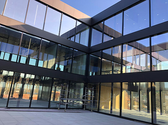 Moderne Glasfassade eines mehrstöckigen Bürogebäudes mit reflektierenden Fenstern und Baugerüst im Innenhof.