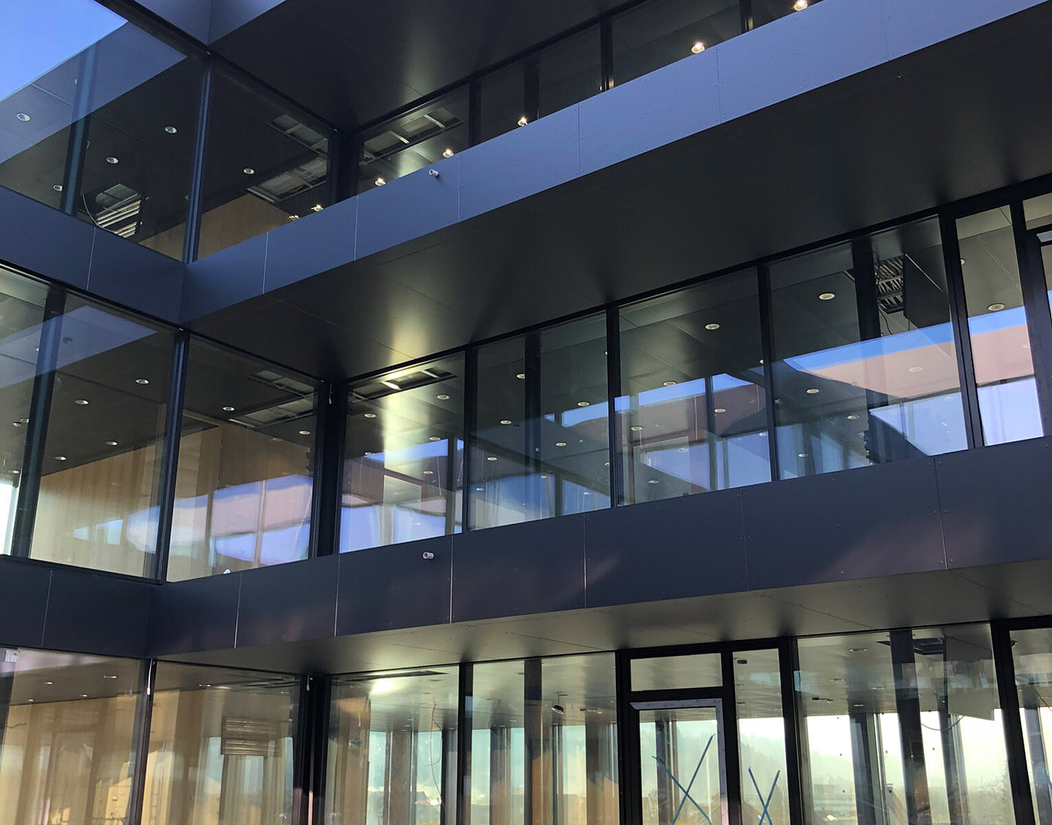 Modernes Gebäude mit großen Glasfenstern und reflexionsarmen Fassaden, das Innenhof mit natürlichem Licht zeigt.
