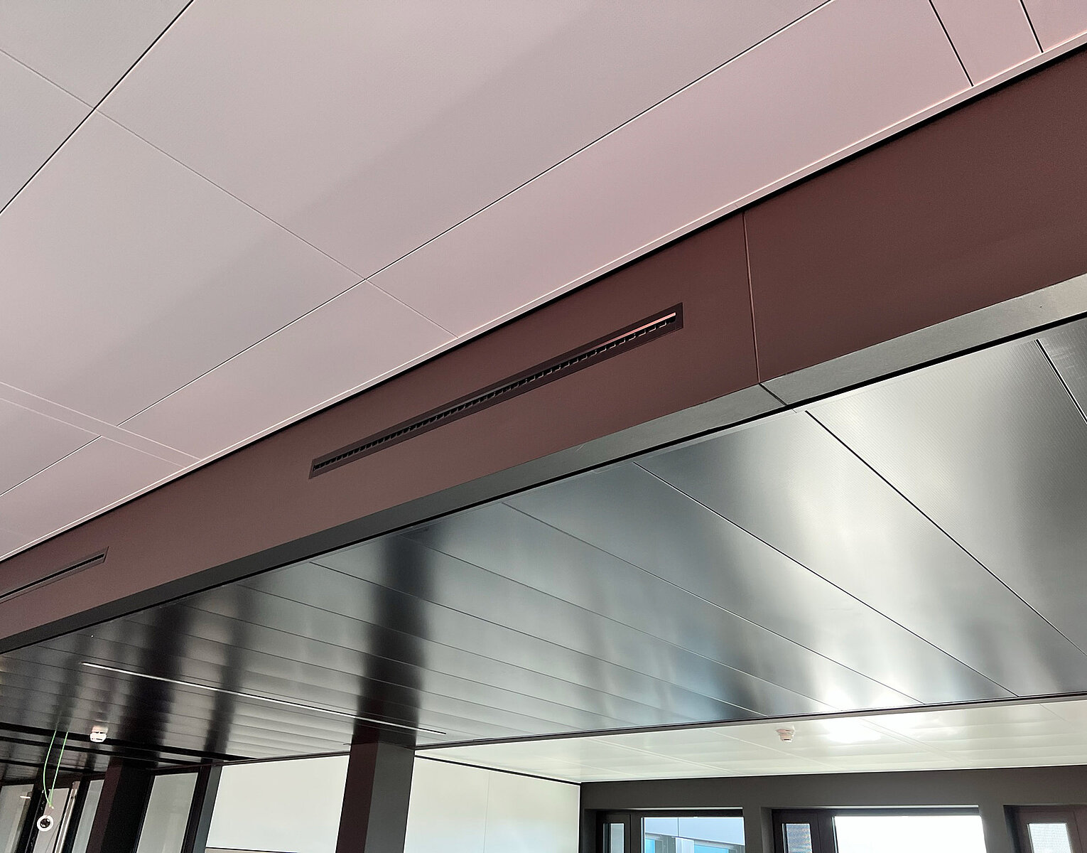 Blick auf eine moderne, dunkle Metall-Decke und einen breiten braunen Balken im Innenraum eines Gebäudes.