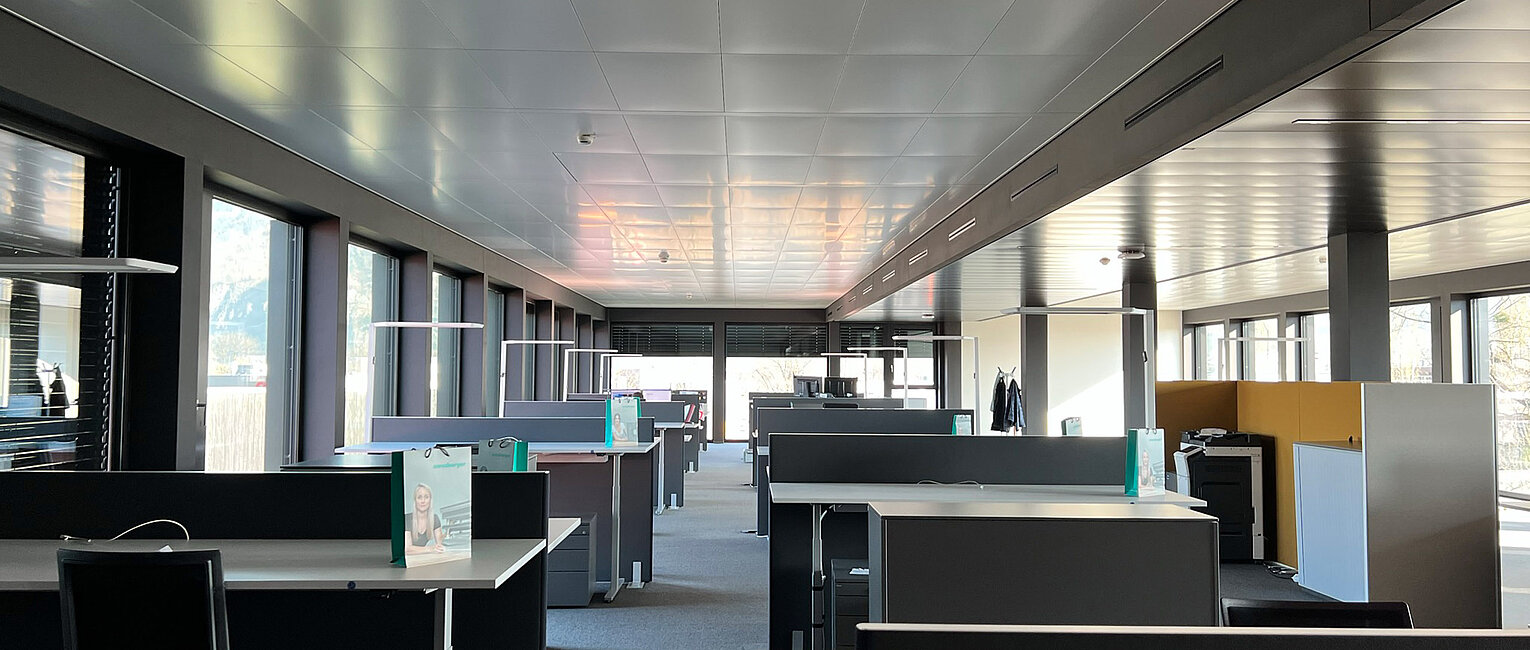 Großes, modernes Büro mit vielen leerstehenden Arbeitsplätzen, Schreibtischen und Trennwänden, natürlichem Licht durch große Fenster und einer neutralen Farbgestaltung.