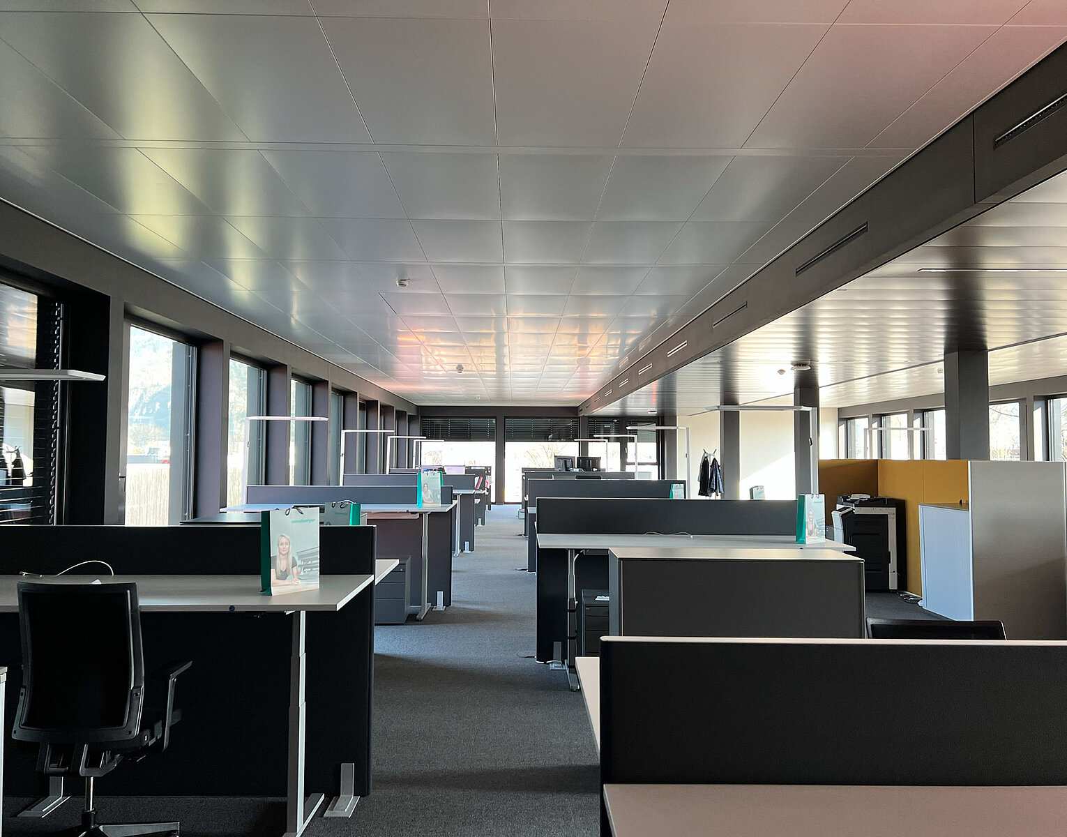 Großes, modernes Büro mit vielen leerstehenden Arbeitsplätzen, Schreibtischen und Trennwänden, natürlichem Licht durch große Fenster und einer neutralen Farbgestaltung.