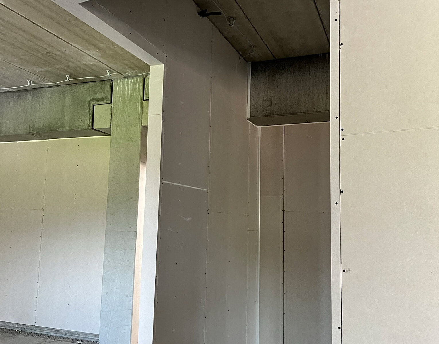 Unfertiger Innenraum mit schlichten grauen Wänden und einer offenen Türöffnung ohne Tür, sichtbar sind Schrauben und Betondecken.